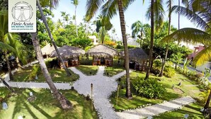A tropical garden with thatched-roof huts, palm trees, and a central pathway. - MINI STUDIOS BEACH (Punta Cana)