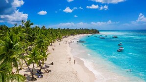 A beach with palm trees, clear blue water, and boats. - MINI STUDIOS BEACH (Punta Cana)