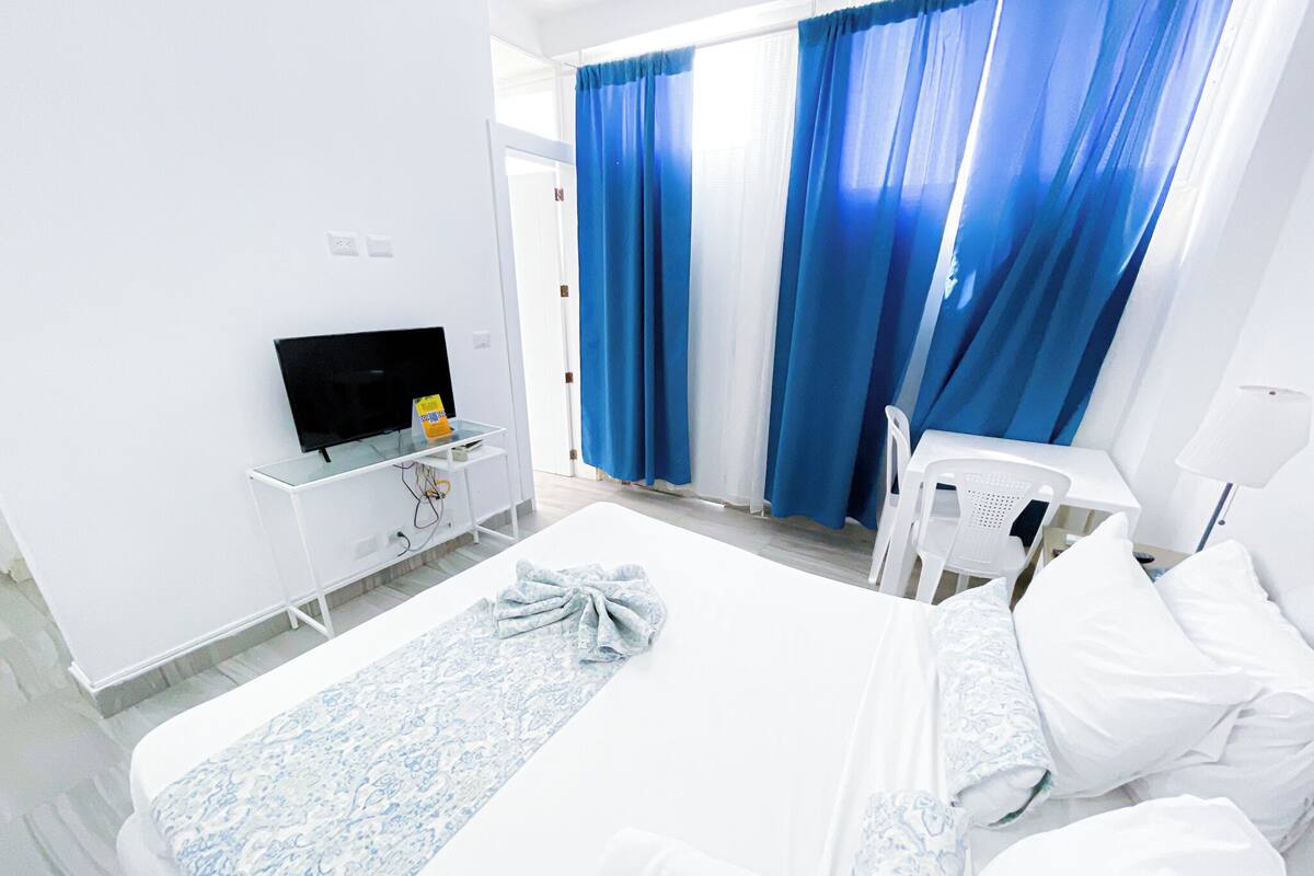 A hotel room with a bed, a TV, a small table, and a chair.