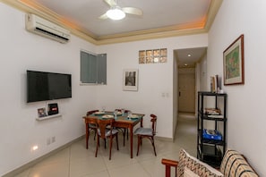 Un comedor con una mesa preparada para cuatro personas, un televisor montado en la pared y un ventilador de techo.