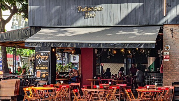 Ravintolassa on ulkoterasseja, sen yllä on kyltti, jossa lukee ”Restaurant Novo”, ja siinä on myös banneri, jossa mainostetaan onnellista hetkeä ja tarjolla olevaa olutta.