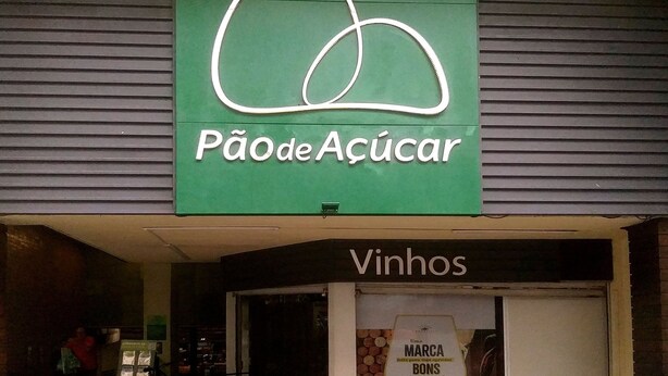 Fachada de loja com um letreiro verde escrito 'Pão de Açúcar' e um aviso abaixo que diz 'Vinhos'.