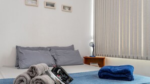 Siististi pedattu sänky, jossa on harmaita ja sinisiä pyyhkeitä, silitysrauta ja yöpöytä, jossa on lamppu.