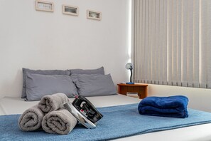 A neatly made bed with grey and blue towels, an iron, and a bedside table with a lamp. - Plaza Copacabana - Conforto e Praia. (Rio de Janeiro)