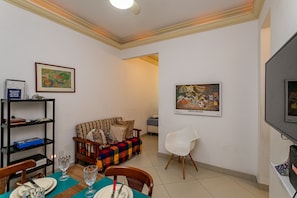 Ein Wohnzimmer mit einer Couch, einem Esstisch, Stühlen, einem Fernseher und Kunstwerken an den Wänden.