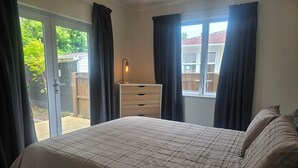 A bedroom with a bed, a dresser, a window with curtains, and a view of the outside.