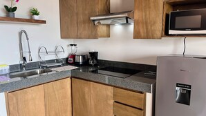 Eine moderne Küche mit Holzschränken, einem Edelstahlkühlschrank, einer Mikrowelle, einem Spülbecken mit Armatur, einem Mixer und einem Toaster.
