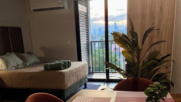 Ein modernes Wohnzimmer mit einer Couch, einem Esstisch mit Stühlen und einem großen Fenster mit Blick auf die Stadt.