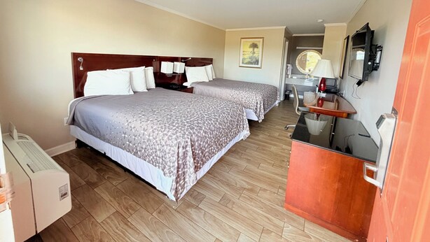 A hotel room with two beds, a desk, a chair, a TV, and a bathroom visible through an open door. - Western Motel (Dawson)