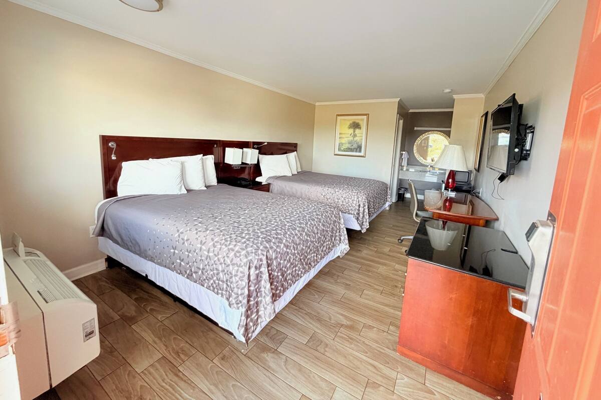 A hotel room with two beds, a desk, a chair, a TV, and a bathroom visible through an open door.