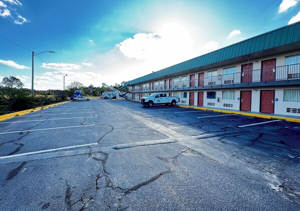 A motel with a row of rooms, a parking lot, and a building with a green roof.
