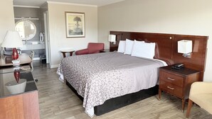 A hotel room with a bed, bedside tables, a desk with a lamp, a chair, and a bathroom visible in the background. - Western Motel (Dawson)