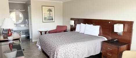 Habitación de hotel con cama, mesitas de noche, escritorio con lámpara, una silla y un baño a la vista.