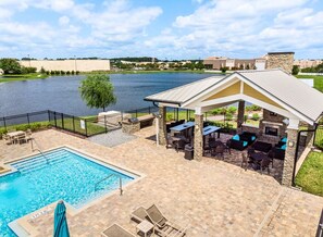 Zona de piscina con terraza cubierta, mobiliario exterior y vistas a un lago.