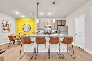Una cocina moderna con una isla central, taburetes de bar y una pared de acento amarilla.