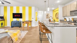 Une cuisine moderne dotée d’un coin bar, d’une table de baby-foot et d’un téléviseur diffusant du contenu « NETFLIX ».
