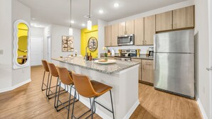 Une cuisine moderne dotée d’un îlot central, d’appareils électroménagers en acier inoxydable et de meubles en bois.
