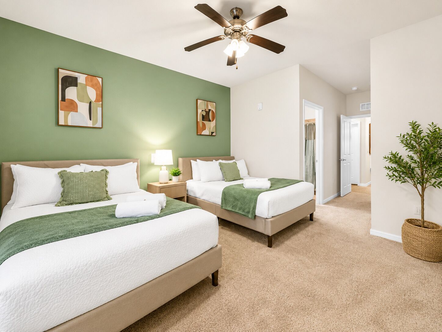 A hotel room with two beds, a ceiling fan, a green wall, and a plant.