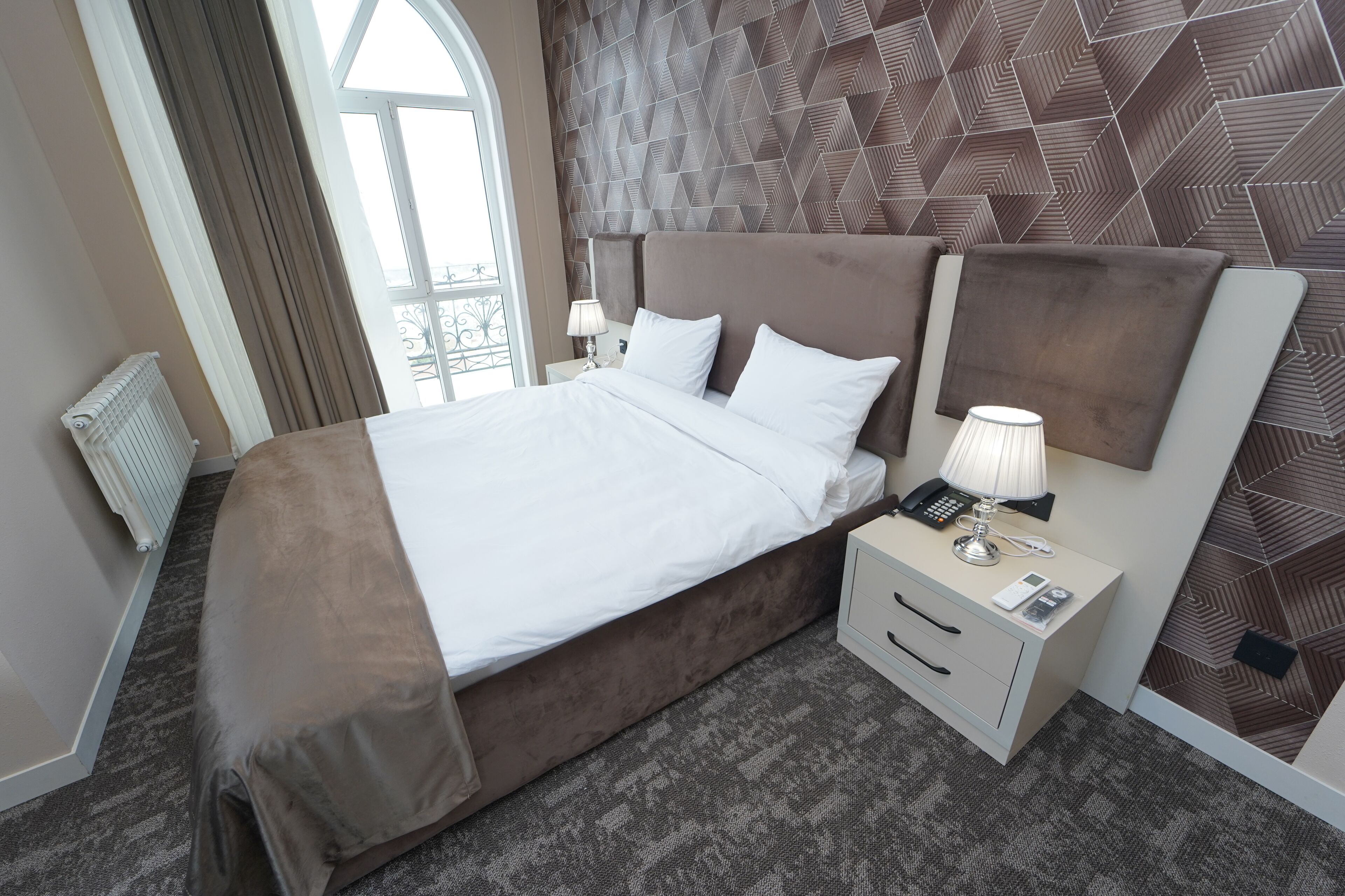 A hotel room with a large bed, a bedside table with a lamp, and a patterned wall.