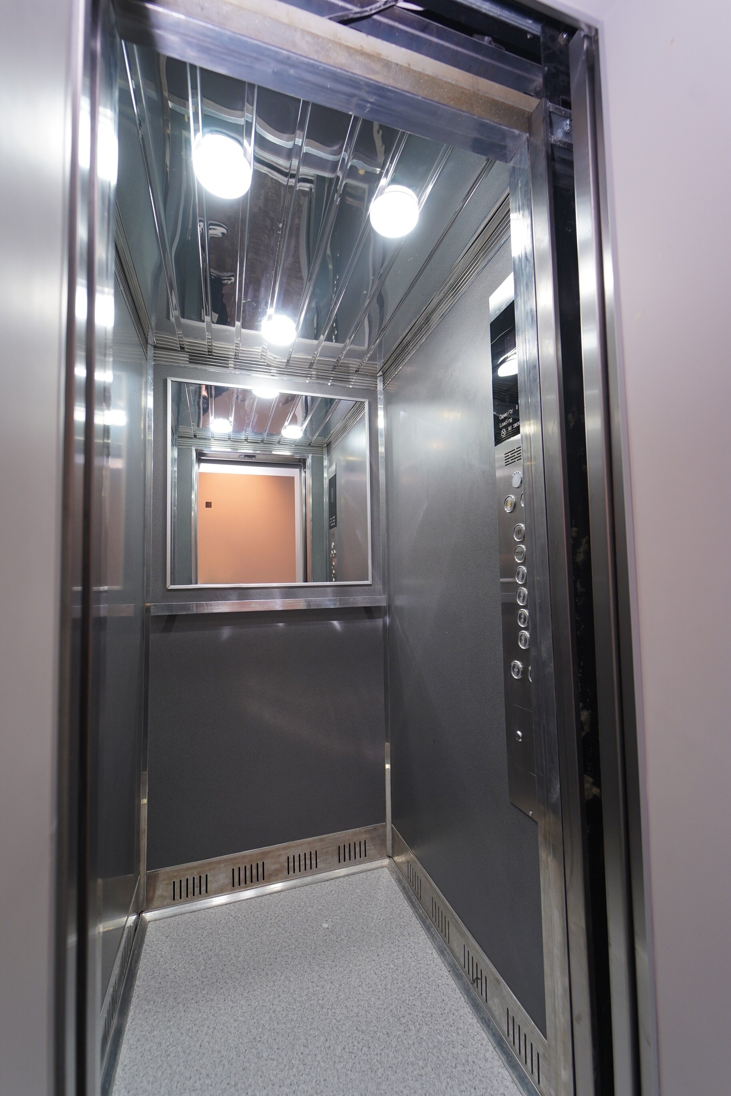 An elevator interior with metallic walls, a control panel, and a carpeted floor.