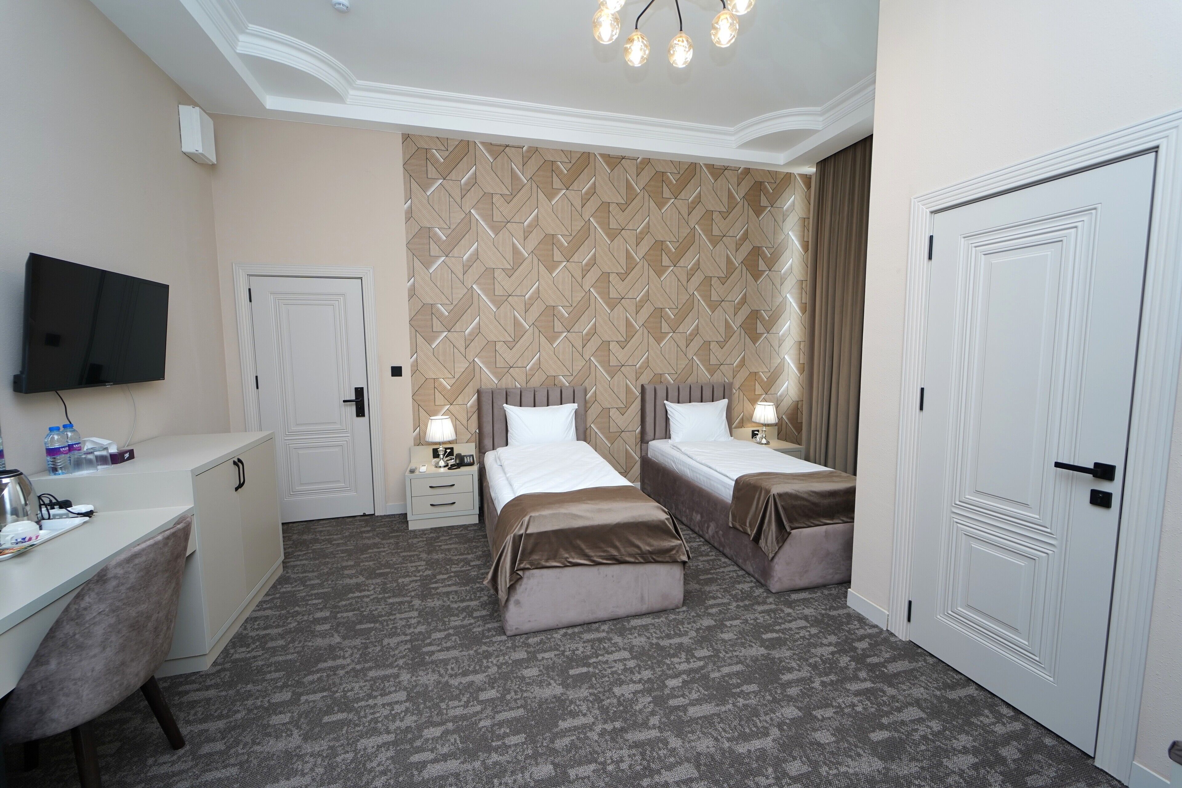 A hotel room with two beds, a desk, a TV, and a patterned wall.