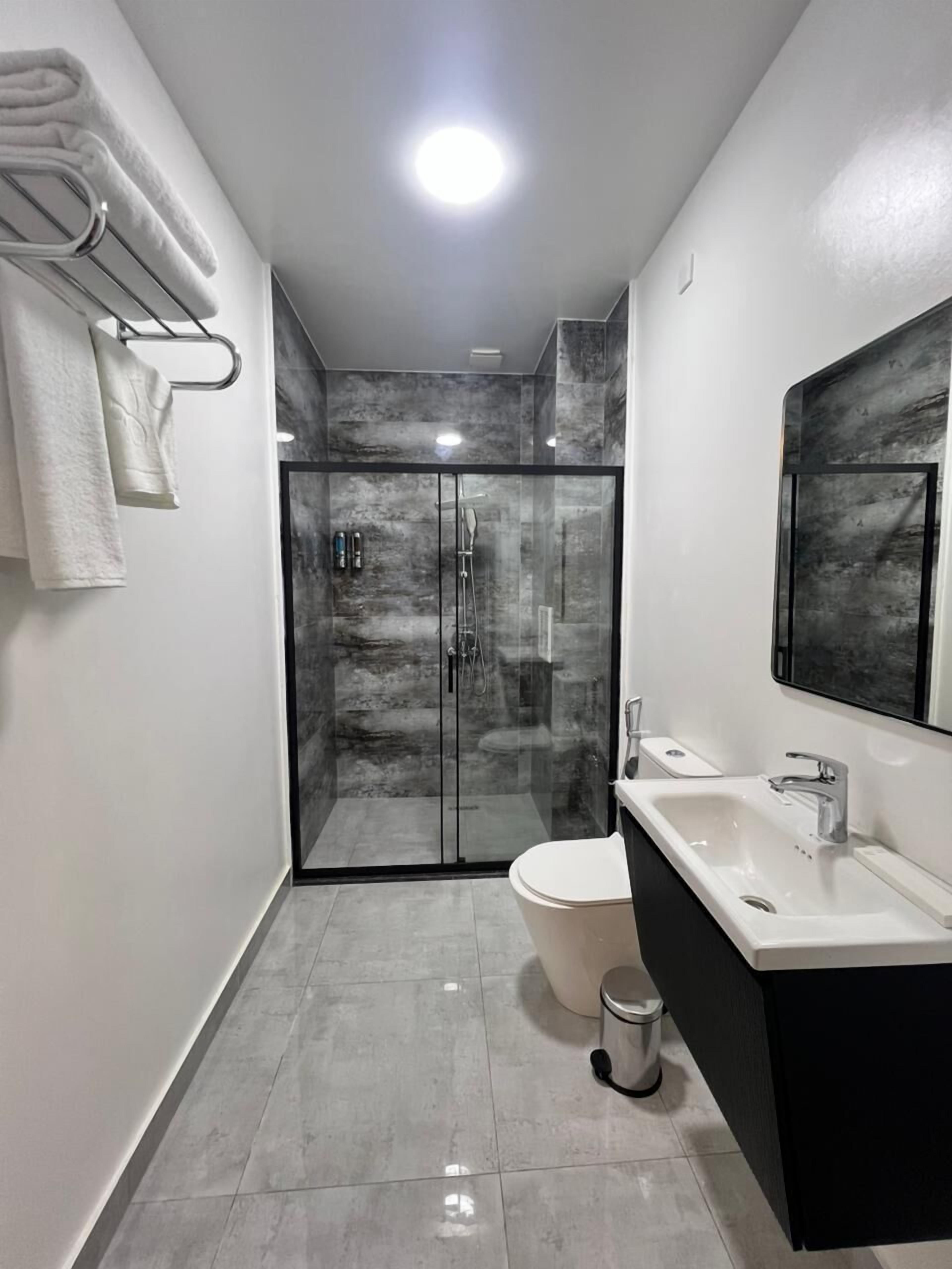 A modern bathroom with a glass-enclosed shower, a white toilet, and a black vanity with a mirror.