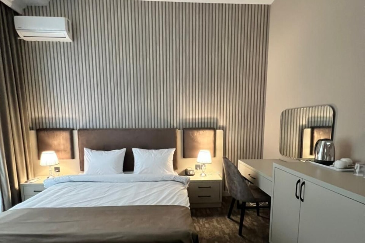 Una habitación de hotel con una cama grande, mesitas de noche con lámparas, un escritorio con una silla y un minibar.