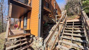 Une cabane en bois dotée d’un balcon, d’un escalier menant à un étage supérieur et d’un petit espace extérieur aménagé pour s’asseoir.