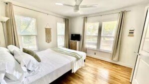 Ein Schlafzimmer mit einem Bett, einem Deckenventilator und großen Fenstern.