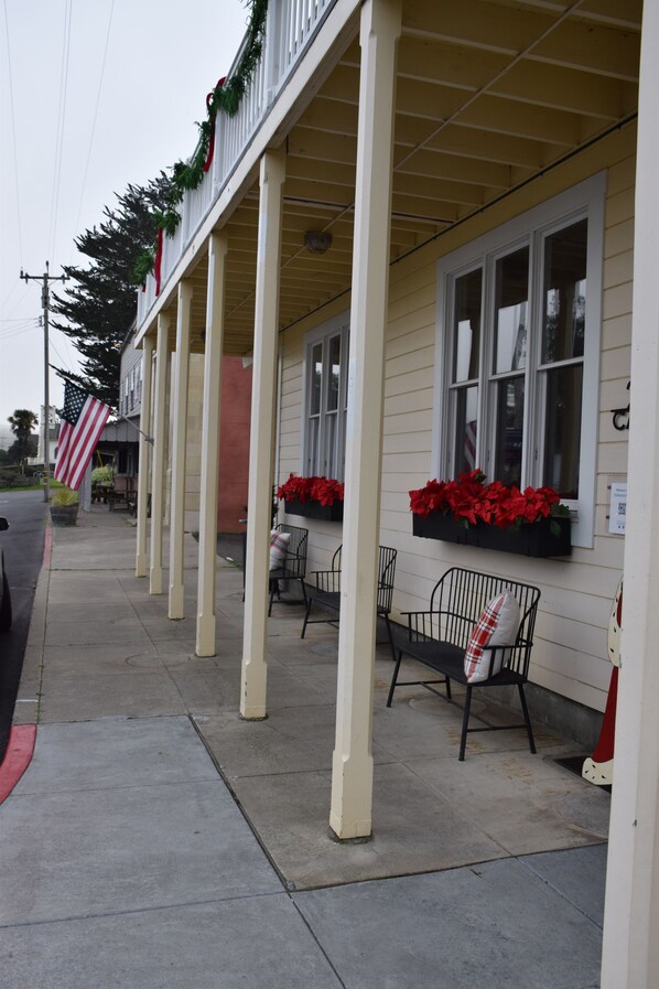 A row of white buildings with a covered porch, red flowers in window boxes, and an American flag on the sidewalk.
