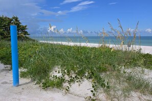 Een strand met wit zand, groene begroeiing en een blauwe paal.