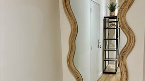 A hallway with a wavy mirror reflecting a door and a plant on a shelf. - Casa Koenig - T2 spacieux & Terrasse en hyper-centre (Brive-la-Gaillarde)
