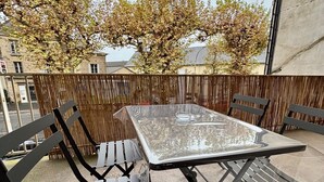 A balcony with a glass table and metal chairs, surrounded by a wooden fence and trees. - Casa Koenig - T2 spacieux & Terrasse en hyper-centre (Brive-la-Gaillarde)