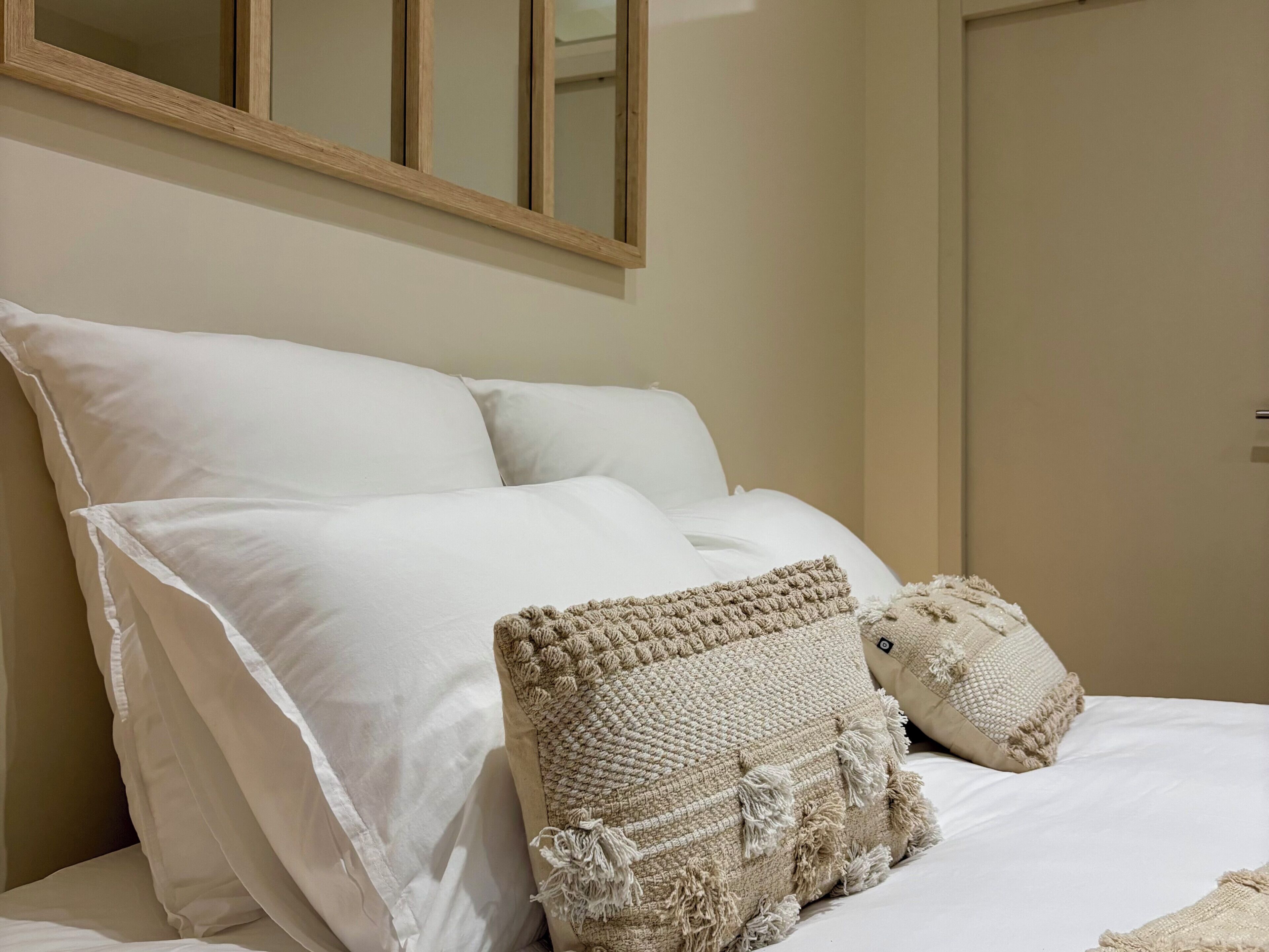 Una cama bien hecha con sábanas blancas y dos almohadas beige con textura.