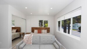 Ein modernes Schlafzimmer mit einem großen Fenster, einem grauen Sofa und einem Bett mit Holz-Kopfteil.