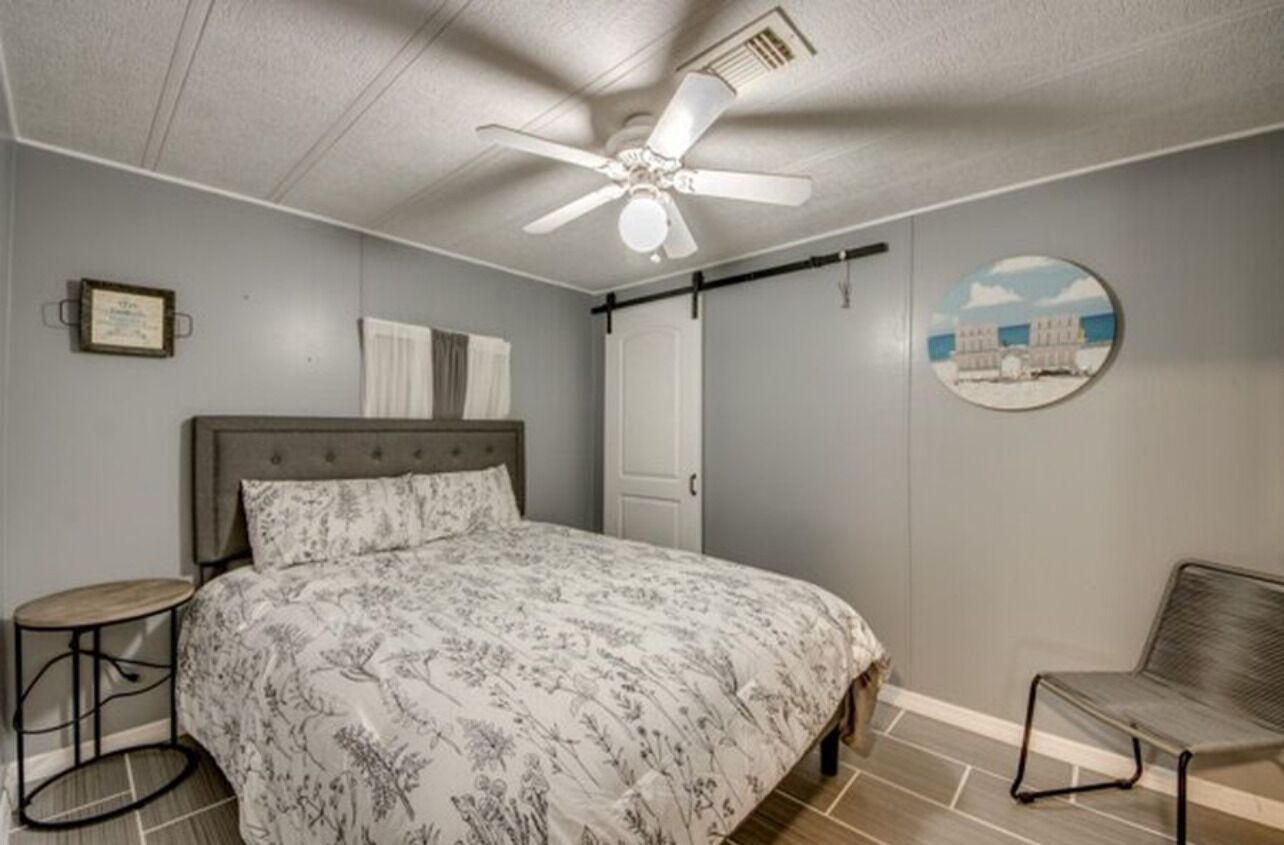 A bedroom with a bed, a ceiling fan, a round mirror, and a framed certificate on the wall.