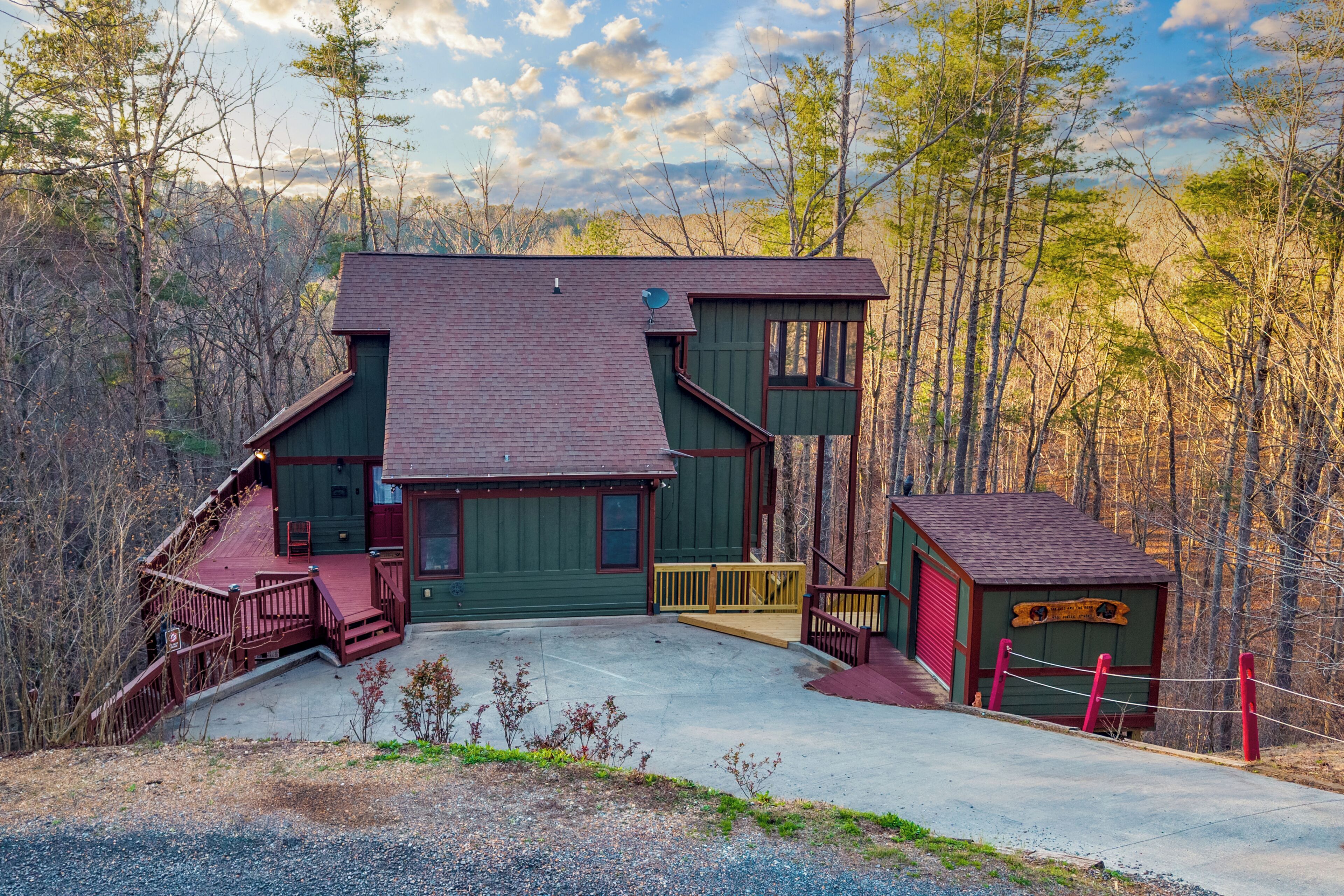 A two-story cabin with a porch, a small shed, and a fenced area.