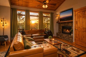 Una sala de estar acogedora con un sofá de cuero, una chimenea, un televisor y un ventanal con cortinas.