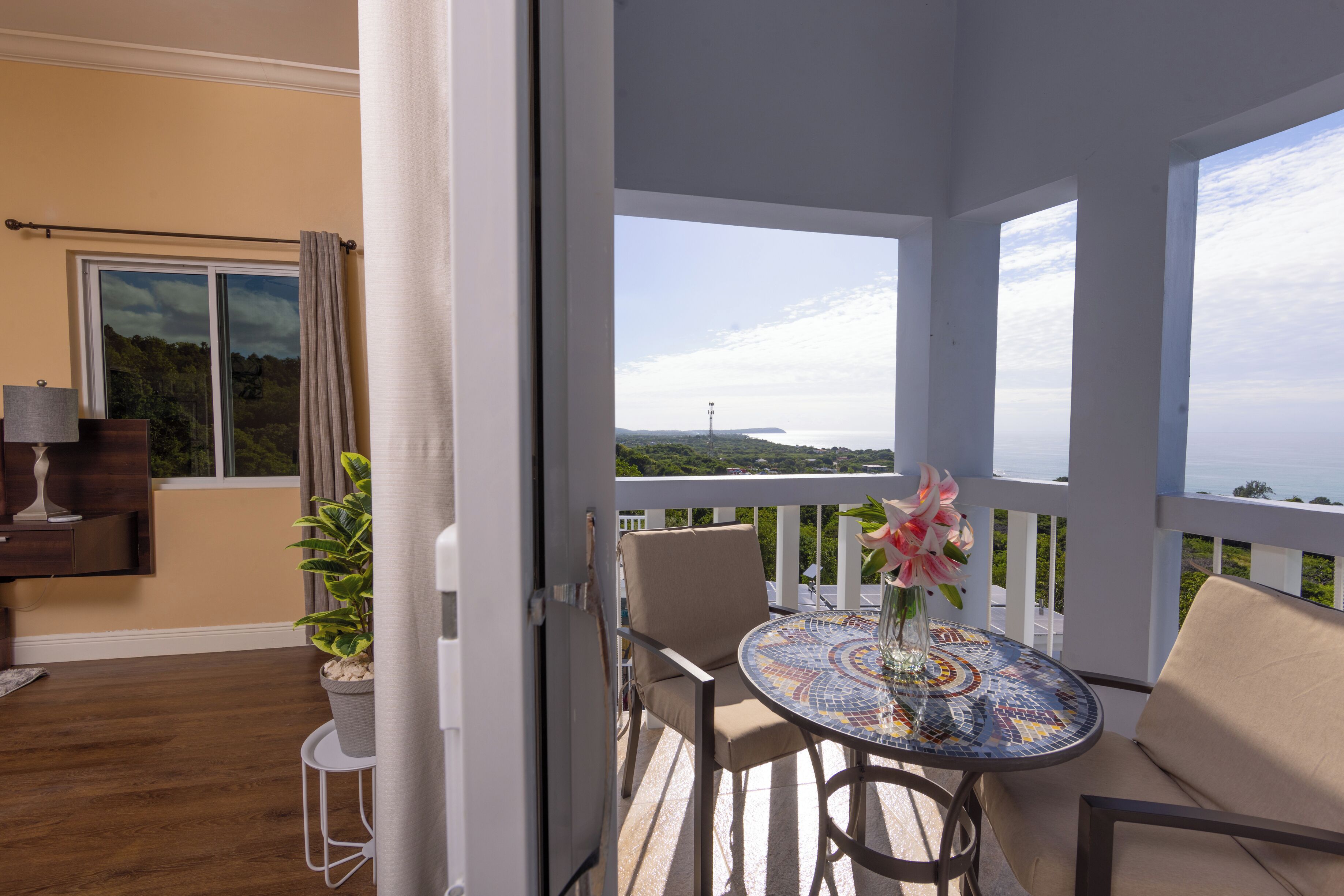 A balcony with a view of the sea, a round table with a vase of flowers, and a chair.
