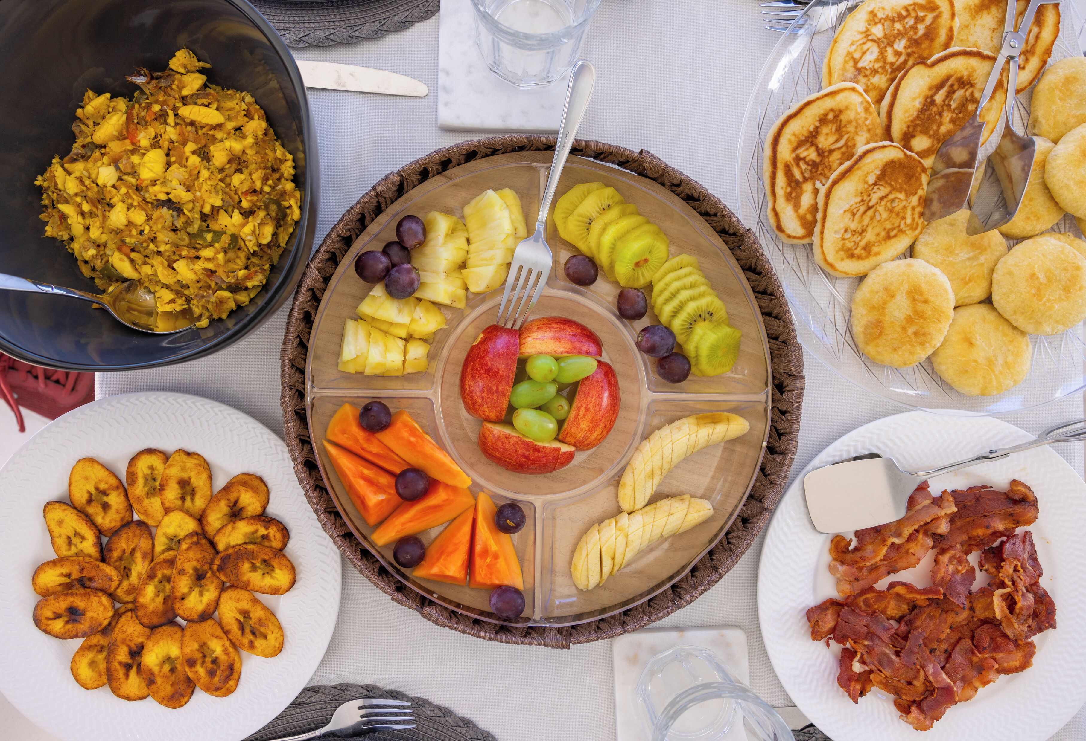 A breakfast buffet with various food items including fruits, pancakes, and bacon.