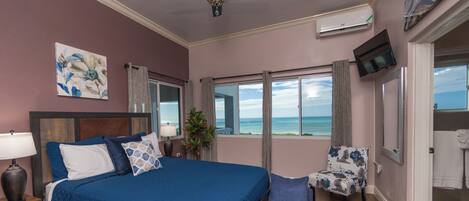 A bedroom with a large bed, a chair, a TV, and a view of the ocean.