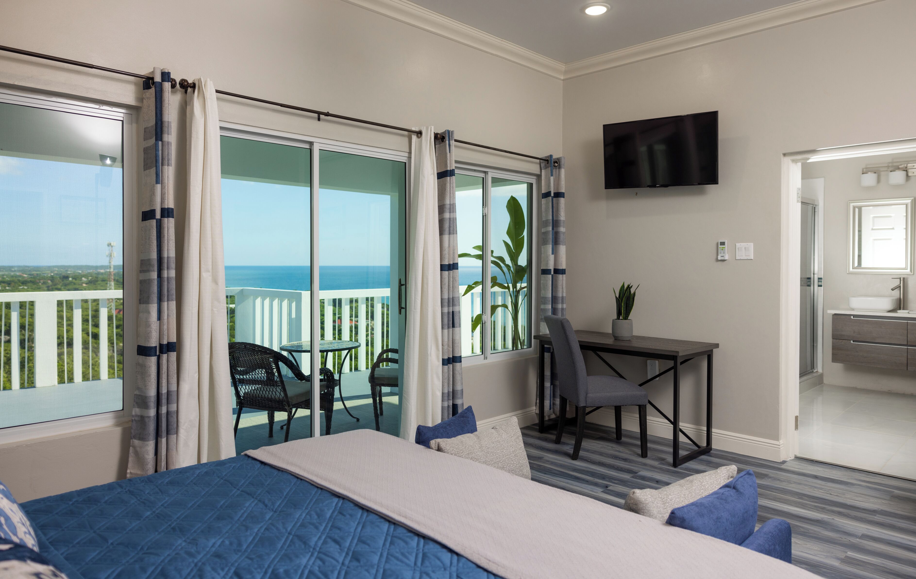 A hotel room with a bed, a desk, a chair, and a balcony with a view of the ocean.