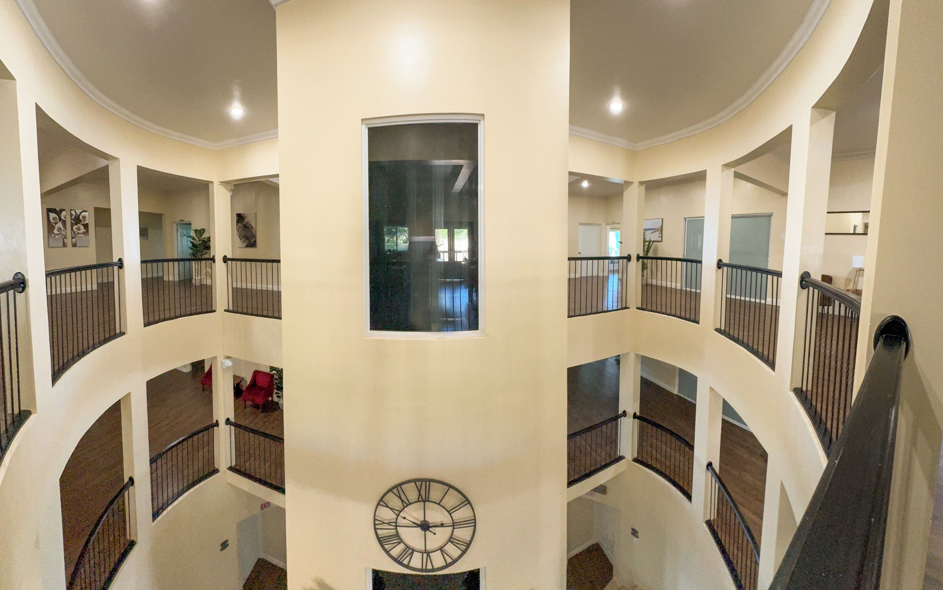 Un interior de varios niveles con un reloj central, balcones curvos y vistas a través de una ventana.