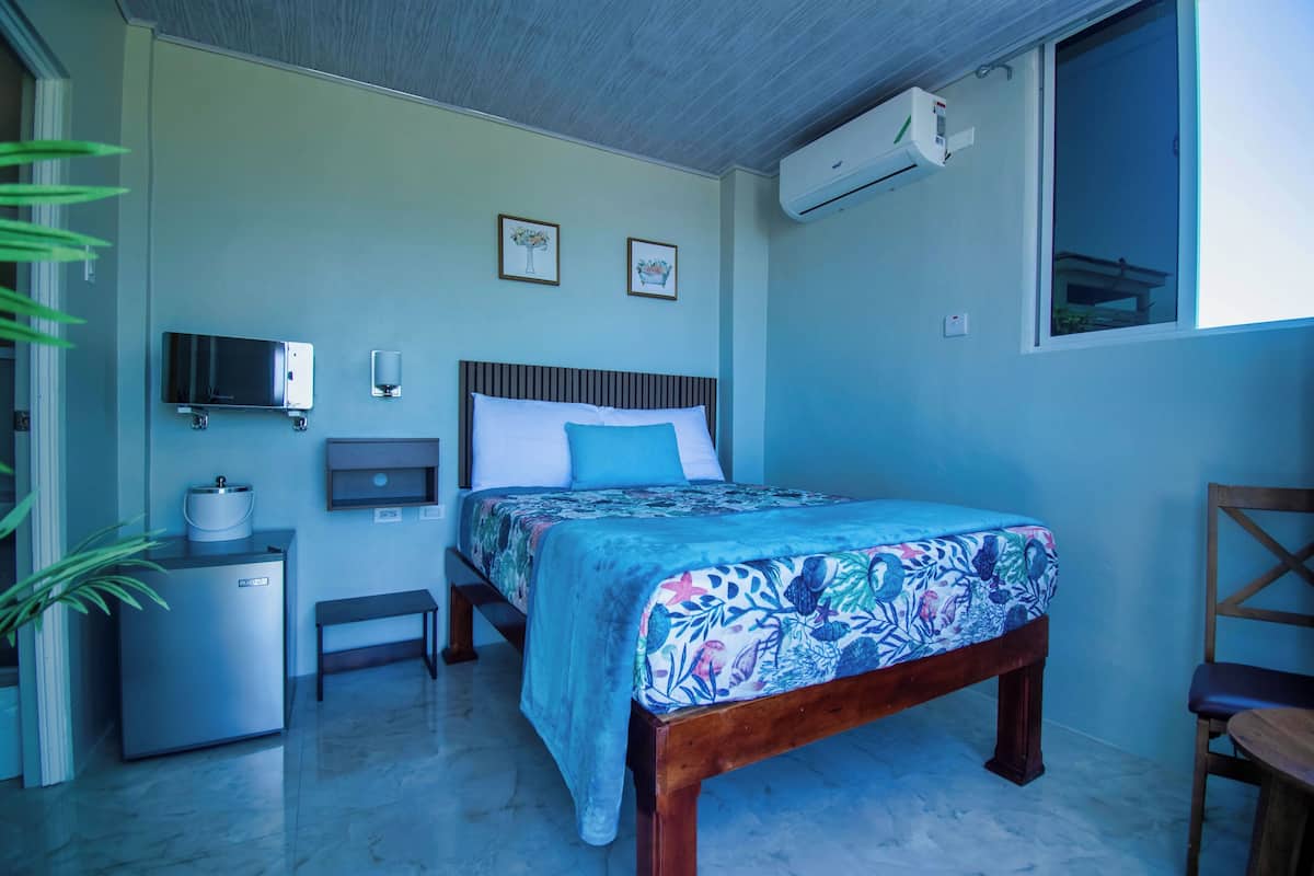 Un dormitorio con cama, un escritorio pequeño, un refrigerador y una ventana.