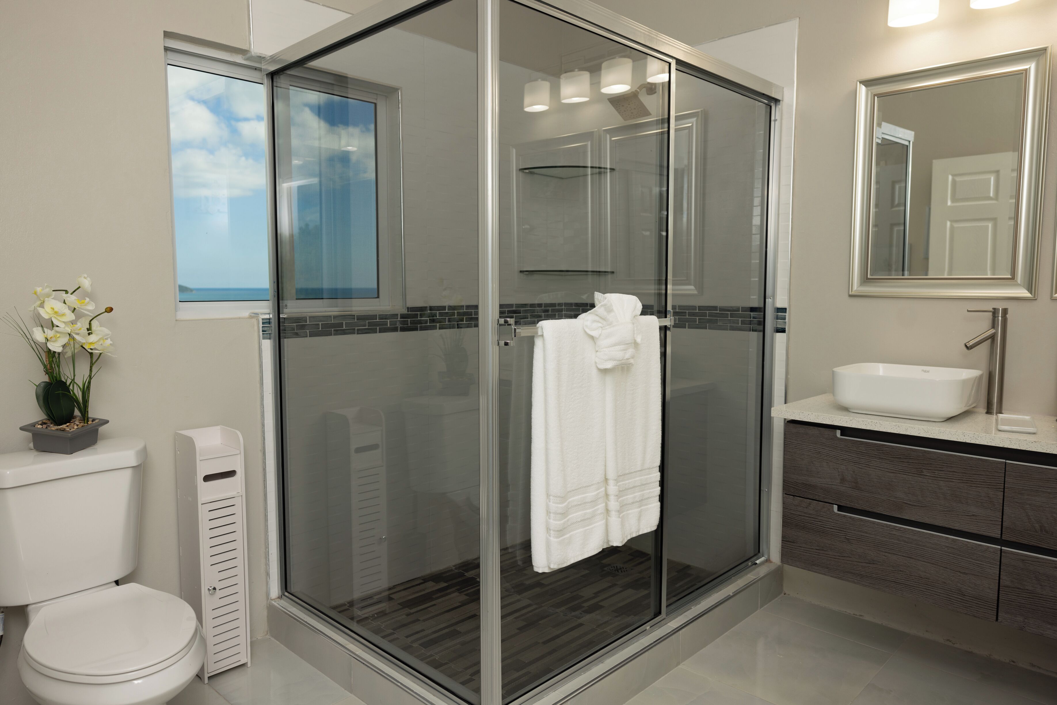 Un baño moderno con ducha de vidrio, inodoro, lavamanos y espejo.