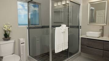 Un baño moderno con ducha de vidrio, inodoro, lavamanos y espejo.