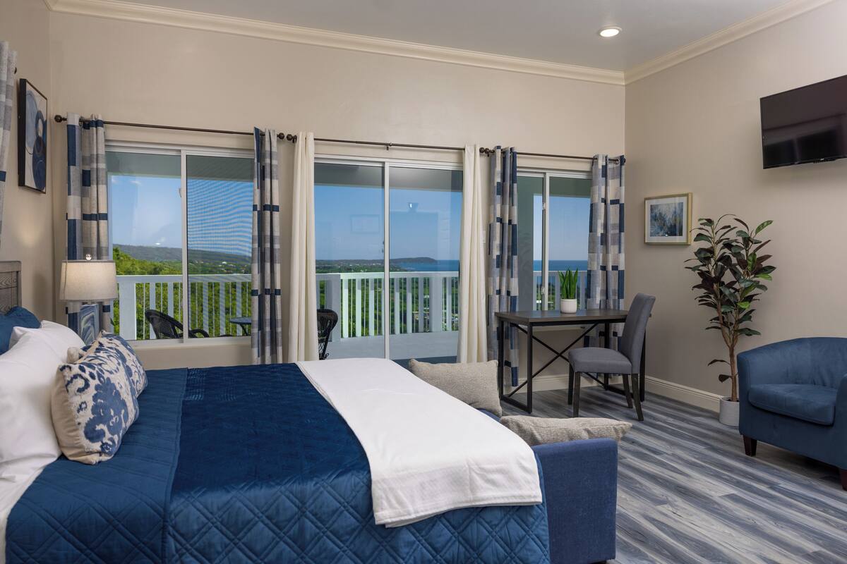 Un cuarto de hotel con una cama grande, un balcón con vistas, un comedor y un televisor montado en la pared.