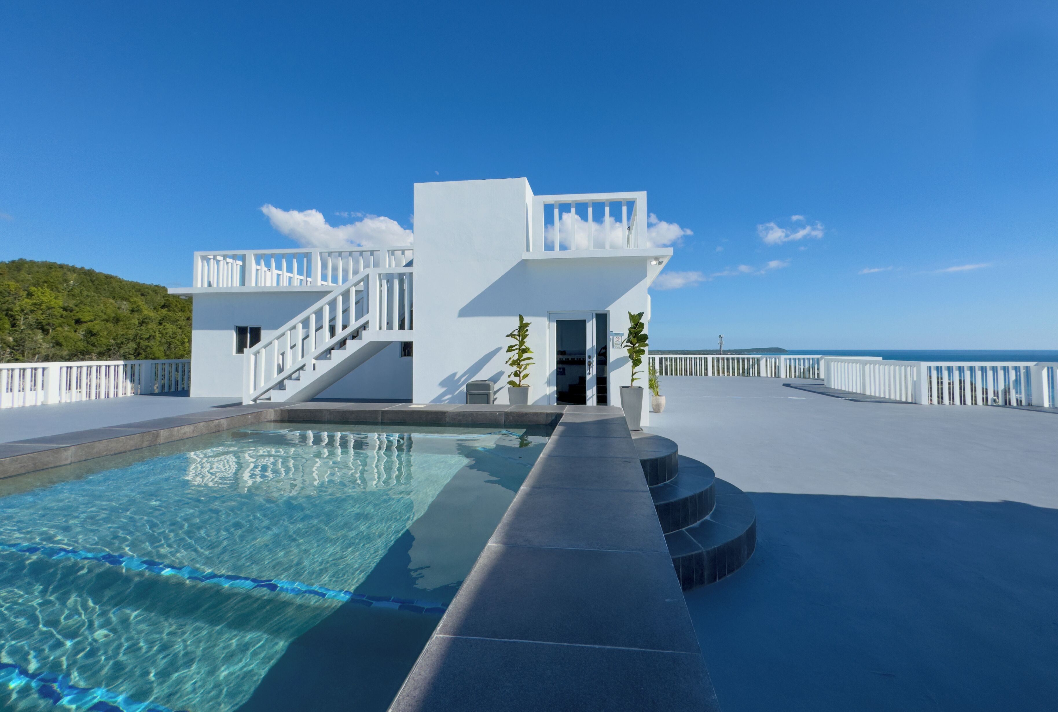 Um edifício moderno com piscina, fachada branca e escadaria que leva a uma varanda.