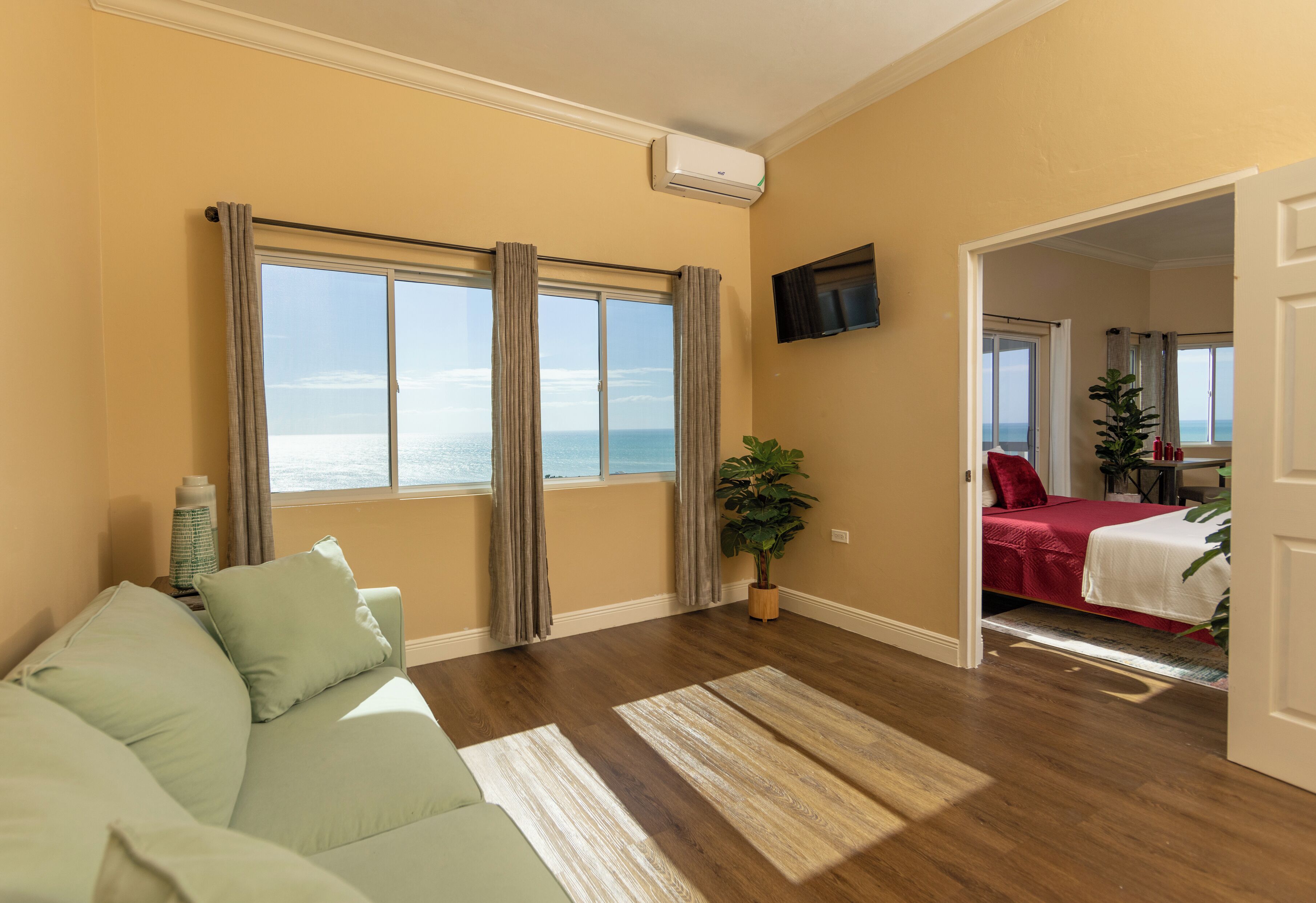 A living room with a large window, a sofa, a TV, and a door leading to a bedroom.