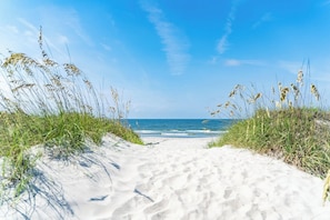 A sandy beach path leading to the ocean, surrounded by grassy dunes. - "Hooked For Life" Cozy 3 Bedroom/2 Bath Getaway w/ Hot Tub. 1 Min. Walk to Beach (Oak Island)